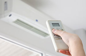 Hand holding remote adjusting a ductless AC unit